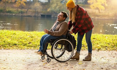 Photo d'une femme poussant son ami en fauteuil roulant dans un parc naturel.